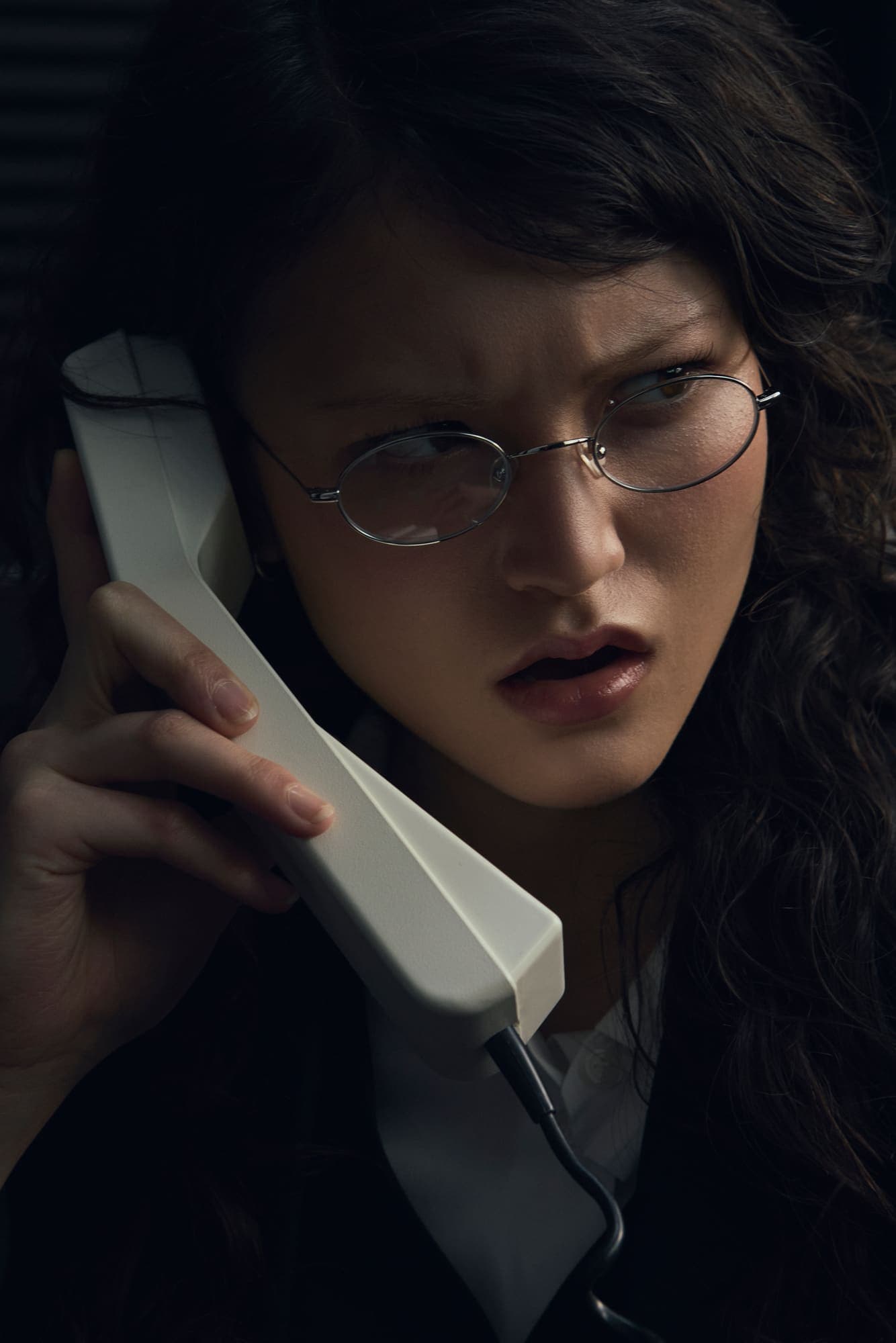 A woman in glasses reacting with disbelief while holding a phone handset