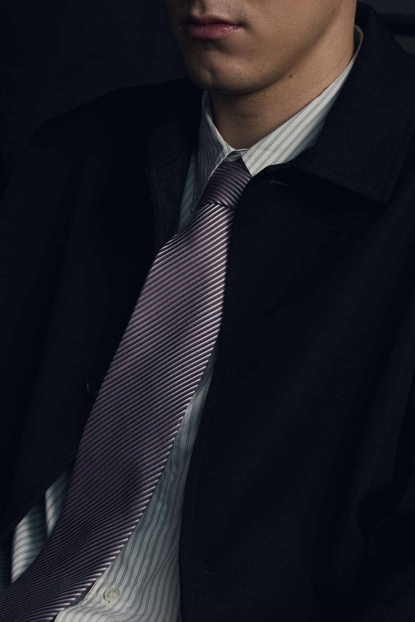 Cropped profile of a man in a dark coat and striped tie, face out of frame