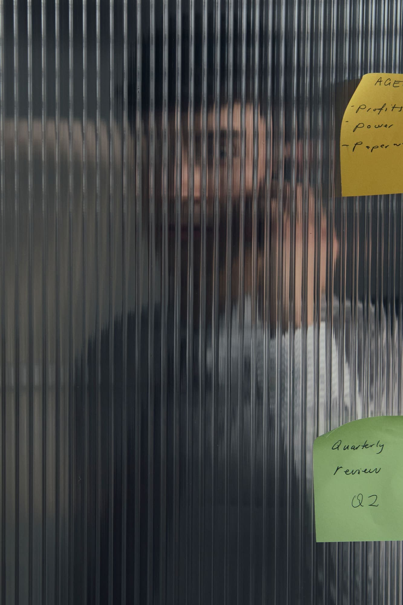 A blurred figure behind reeded glass with a sticky note reading quarterly review Q2