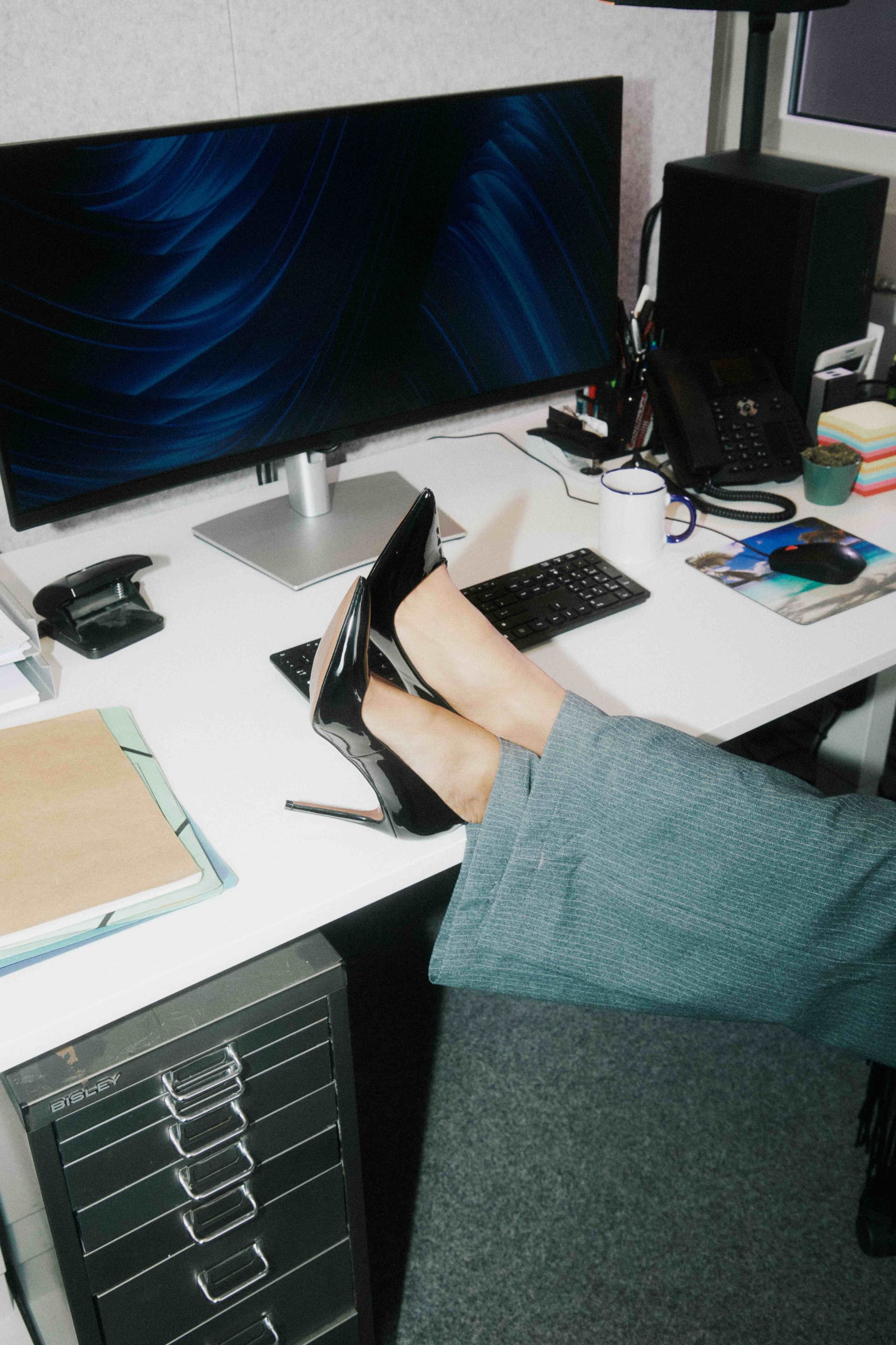 Patent heels propped on a desk beside a keyboard.