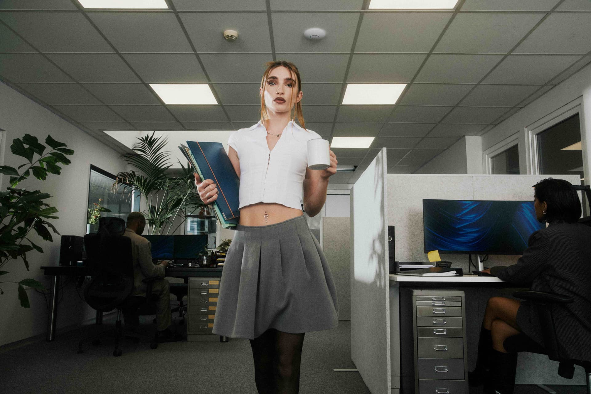 A woman holding a binder and mug facing the camera.