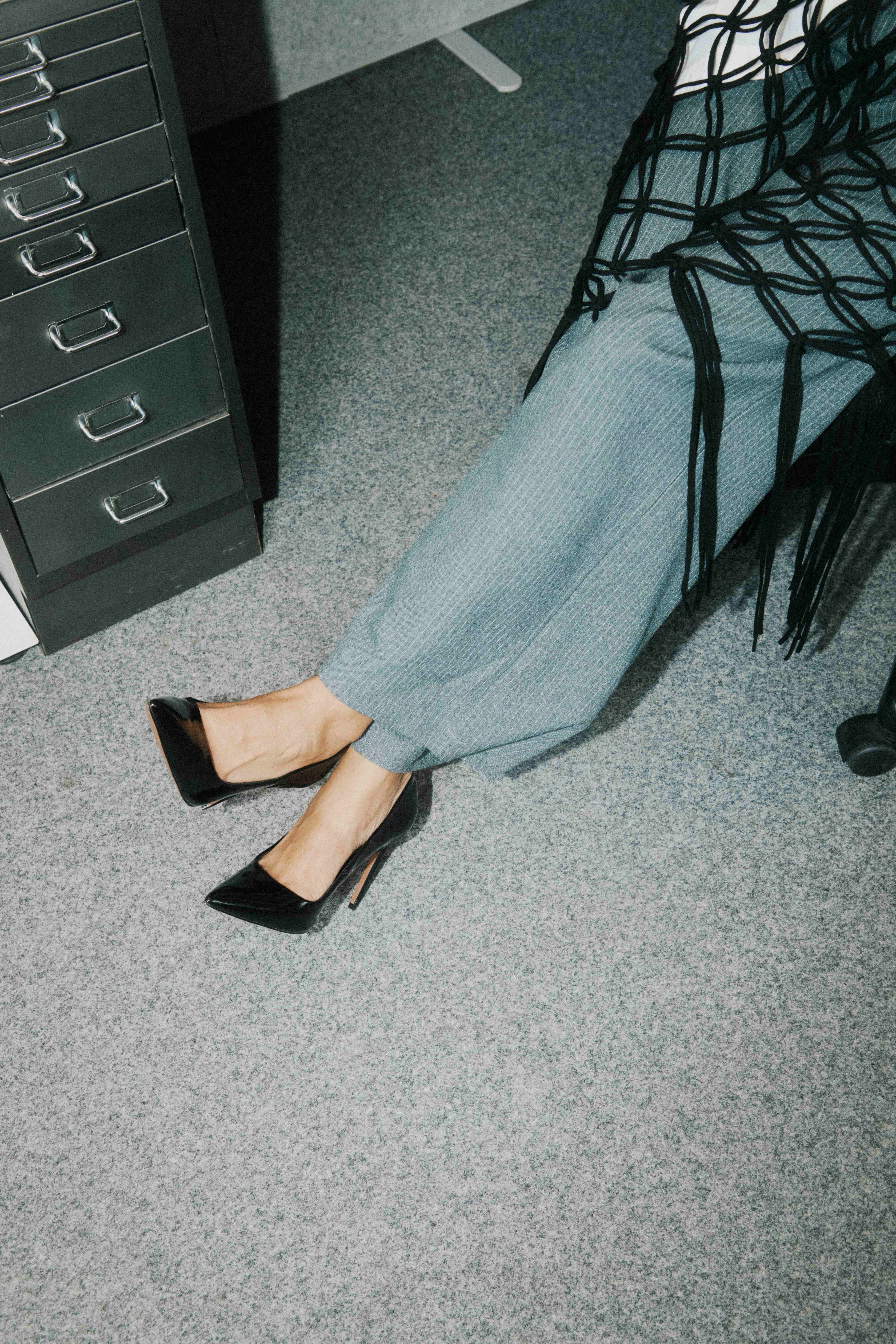 Overhead of black heels on grey carpet beside a metal filing cabinet.