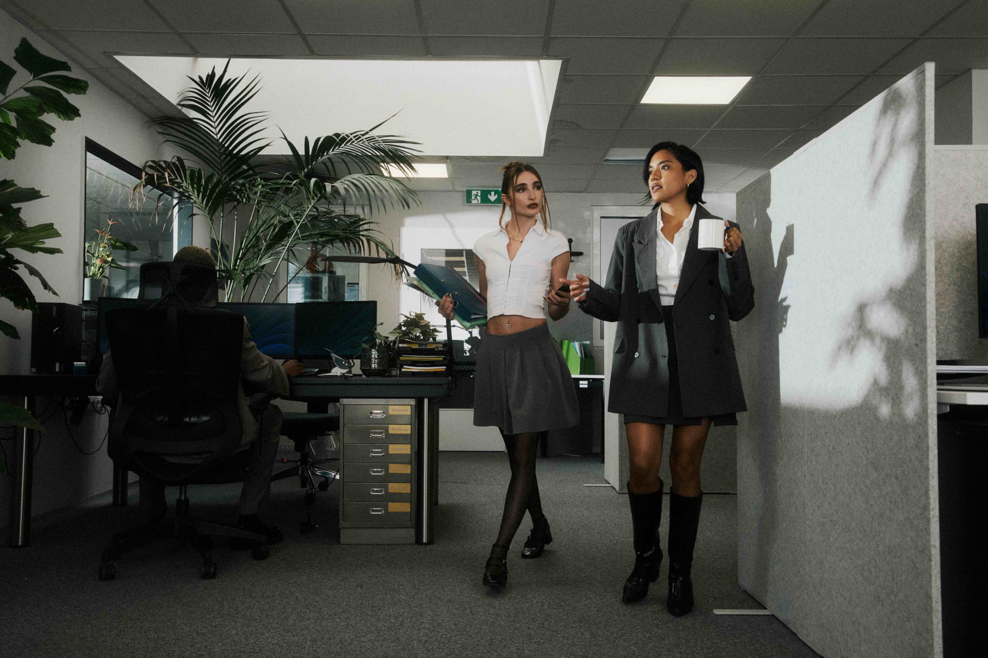 Two women walking through a moody, cinematically lit office.