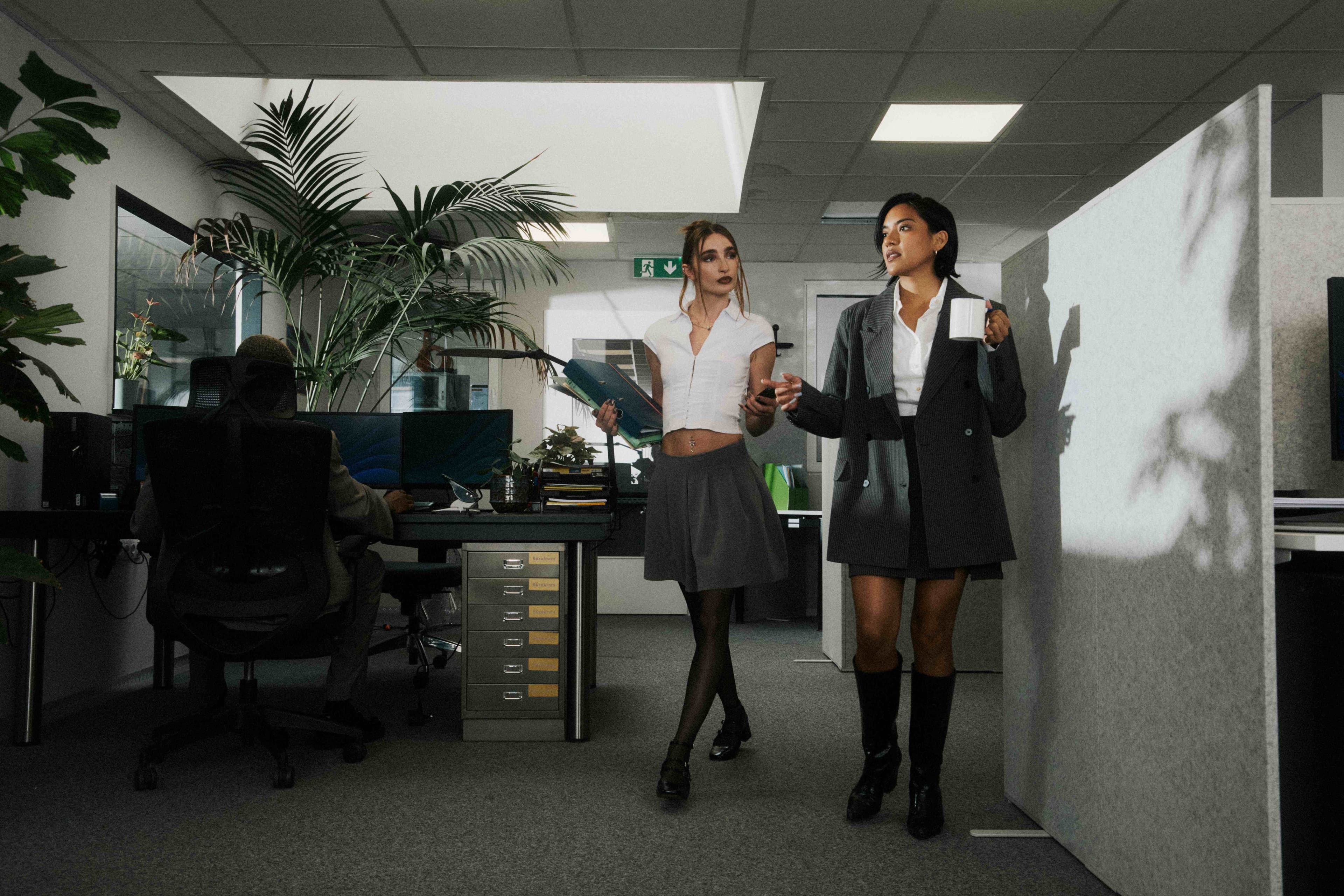 Two women walking through a moody, cinematically lit office.