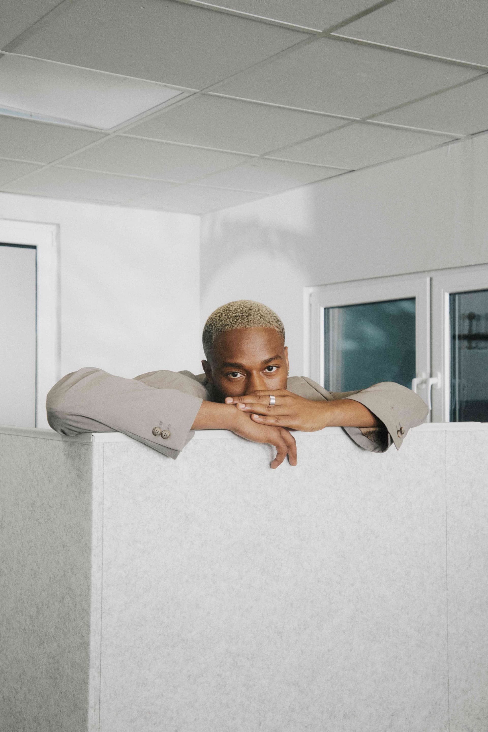 A man resting his chin on folded arms atop a cubicle wall.