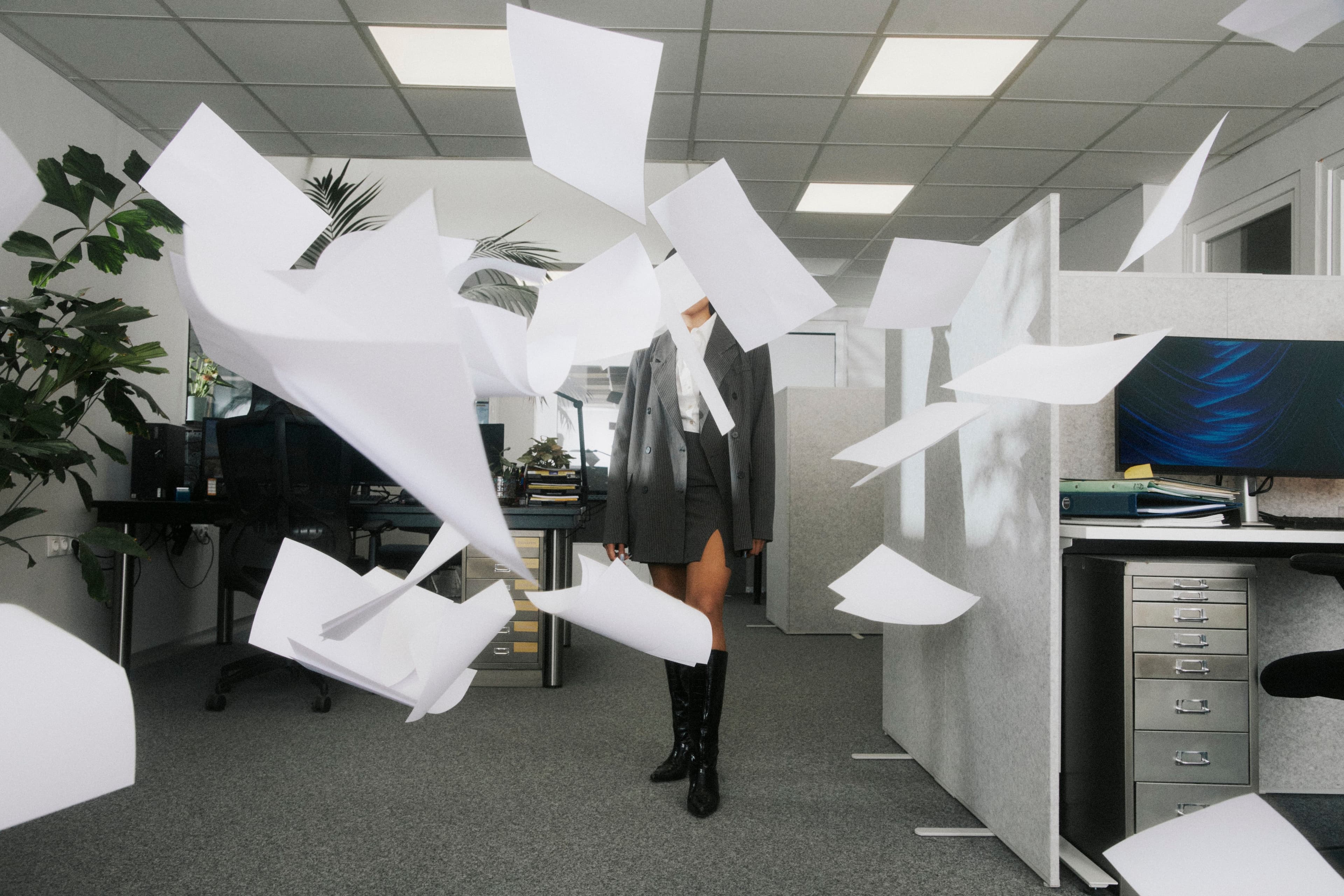 A figure in grey stands amid a burst of flying office papers.