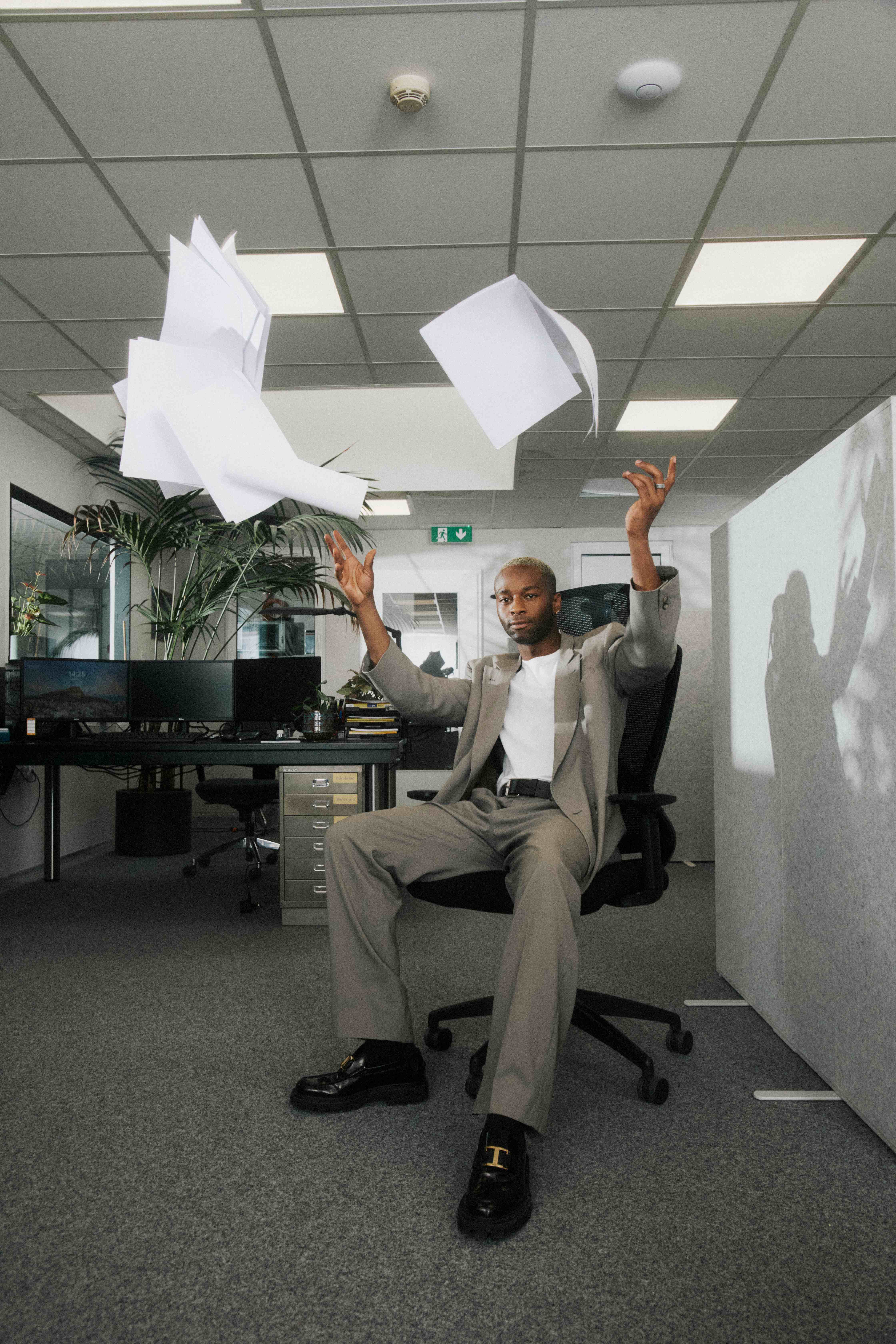 A man reclined in a chair tossing papers overhead.