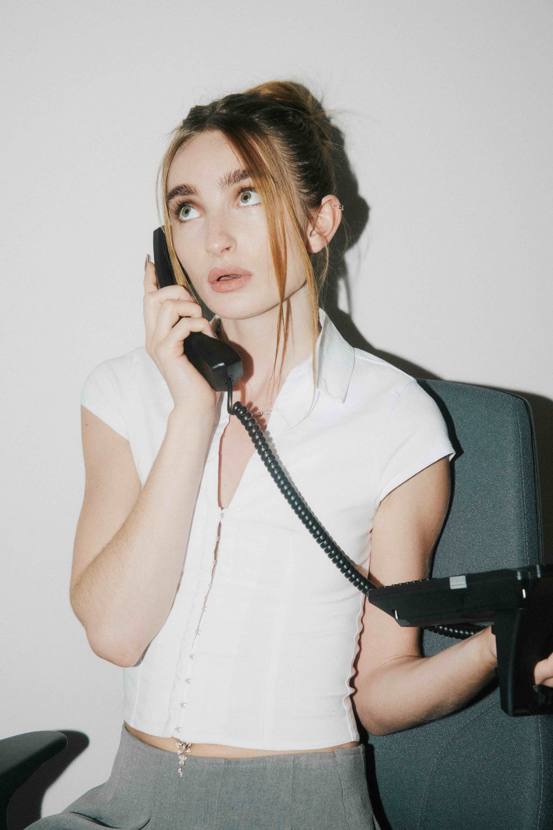 A woman on a corded desk phone looking up.