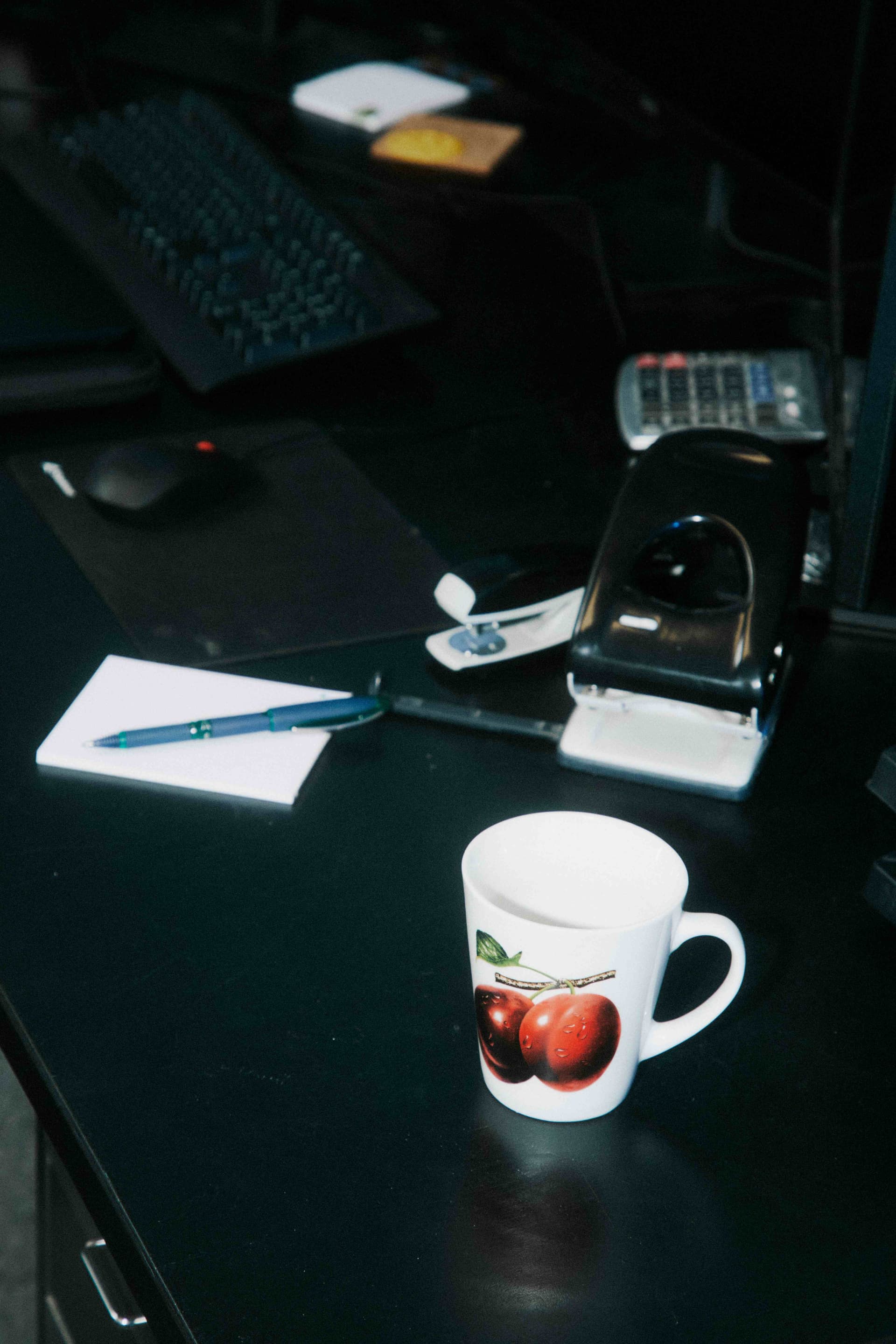 A moody dark desk with a mug, notepad, and pen.