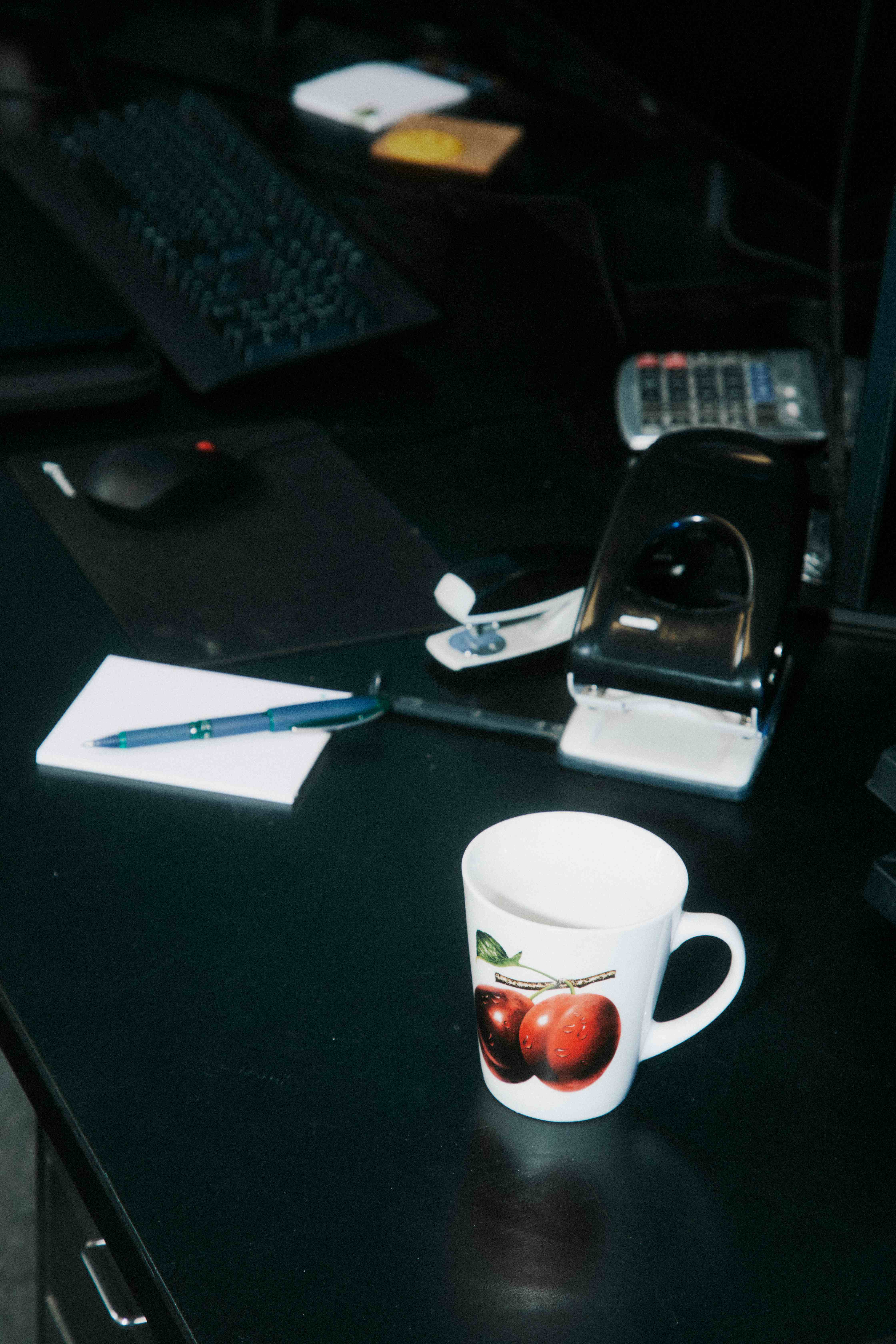 A moody dark desk with a mug, notepad, and pen.