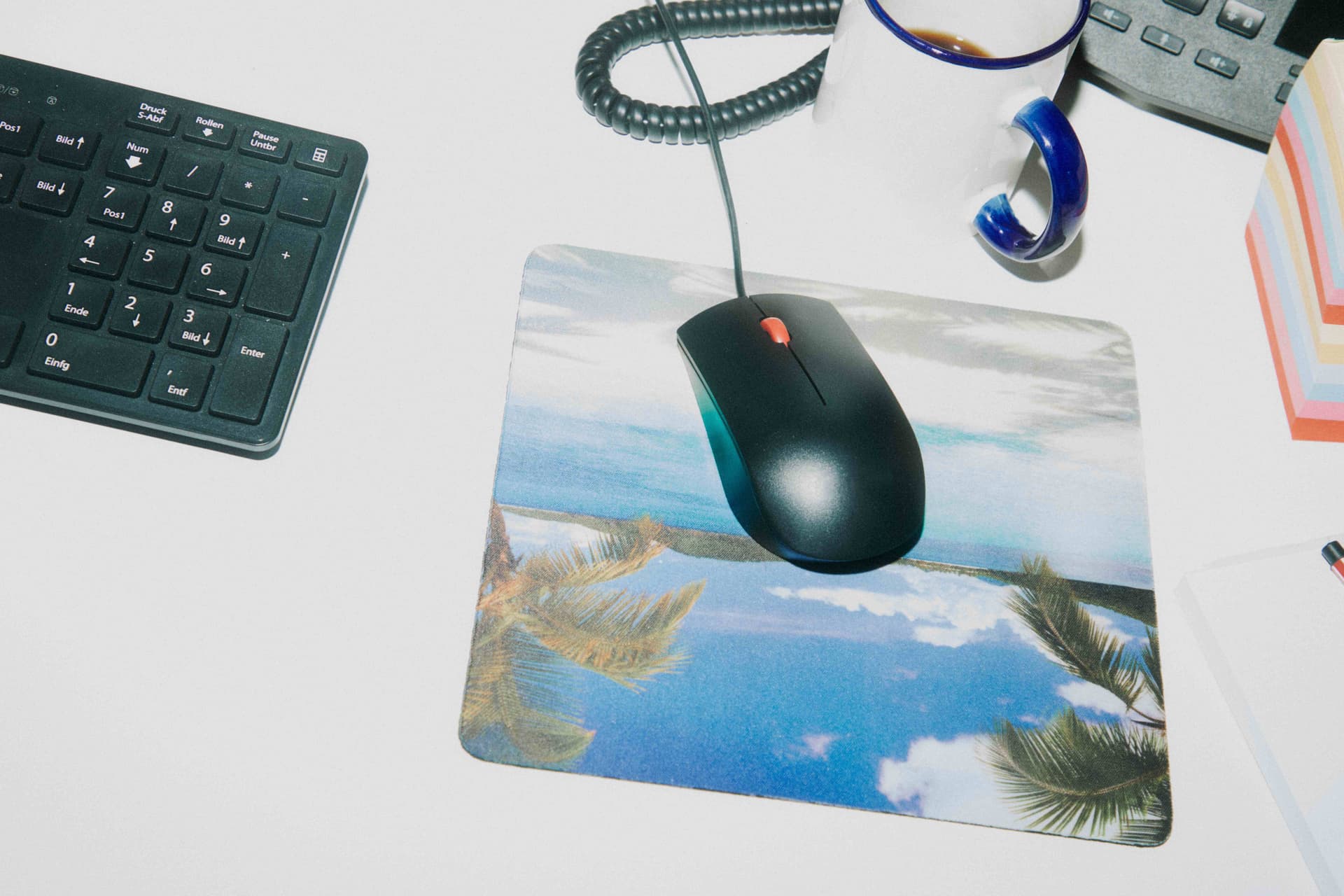 Top-down desk with keyboard, palm-print mousepad, and a coffee mug.
