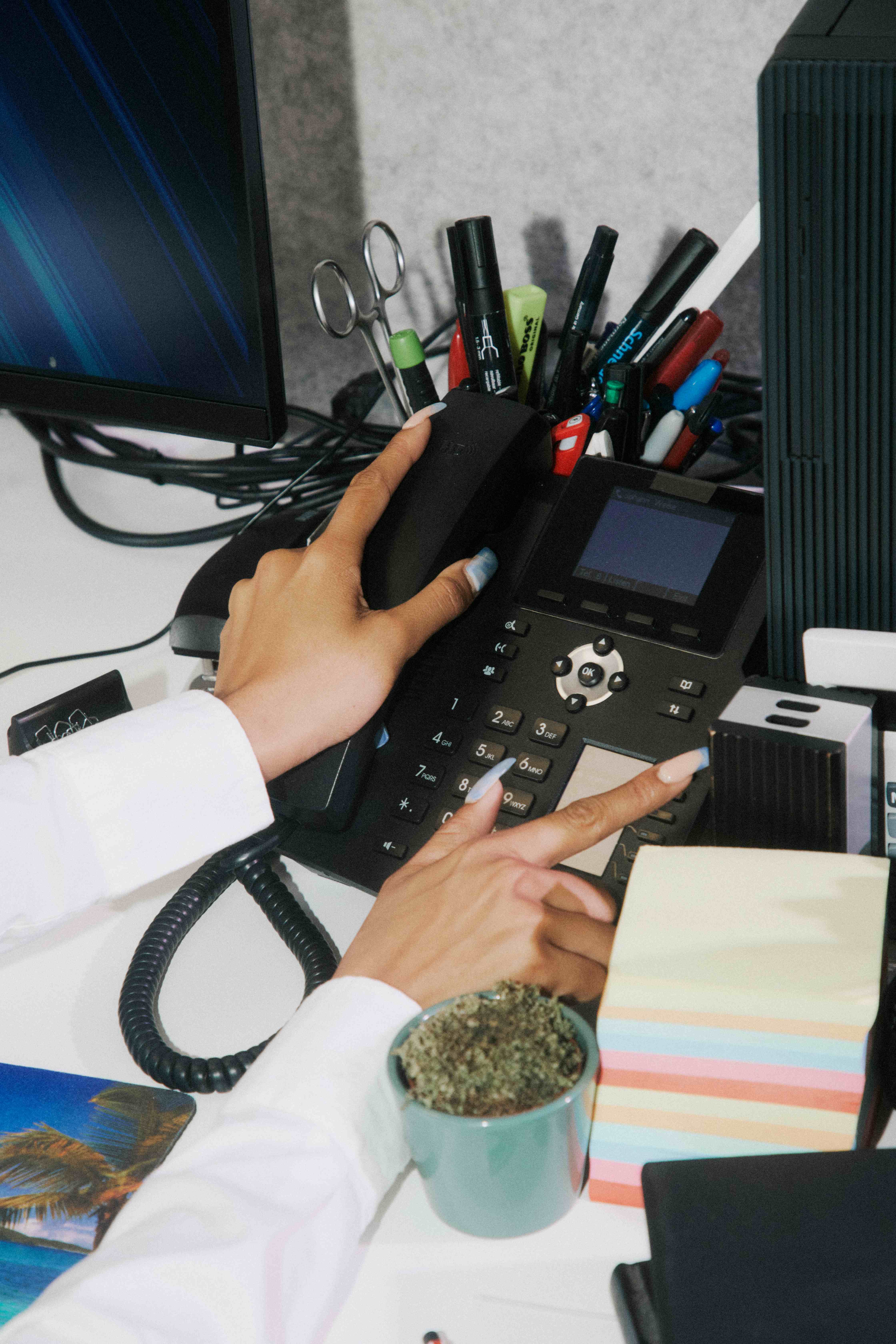 Overhead of hands using a black desk phone.